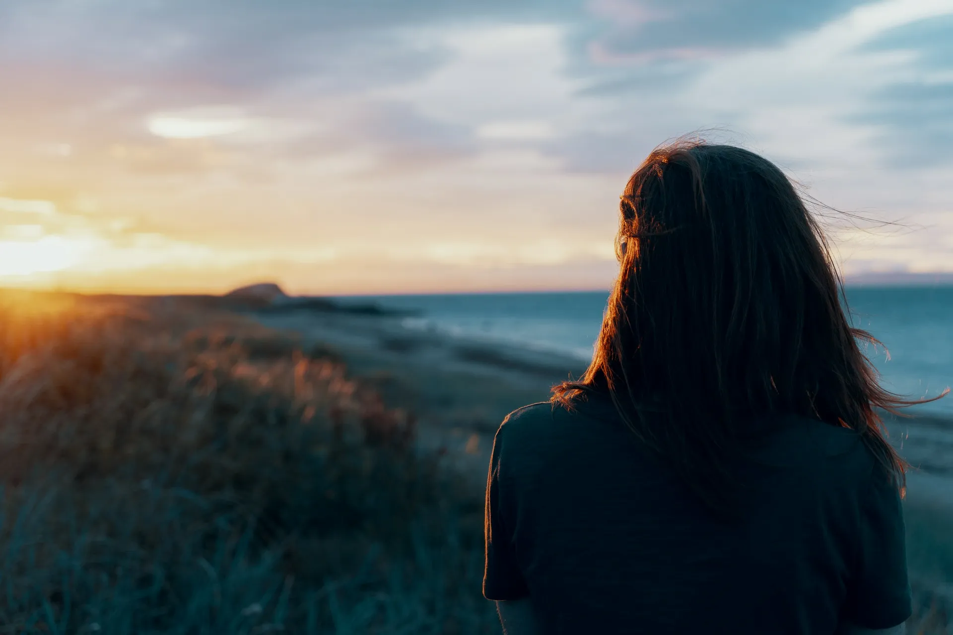 Someone sitting outdoors at dusk, looking out over the coast